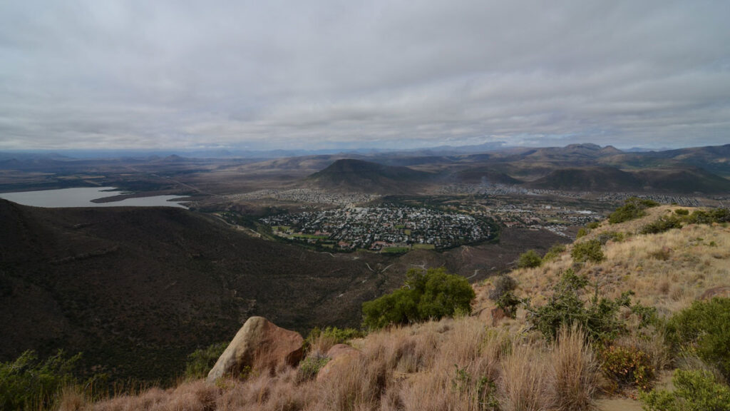 A photo taken from on a hill shows a populated valley surrounded by brown mountains on a cloudy day.
