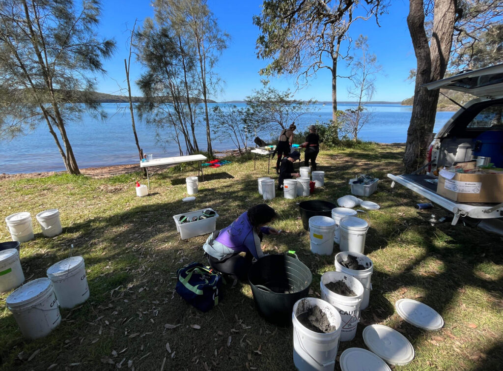 A research team arranges a collection of sediment-filled buckets on the shores of a lake.