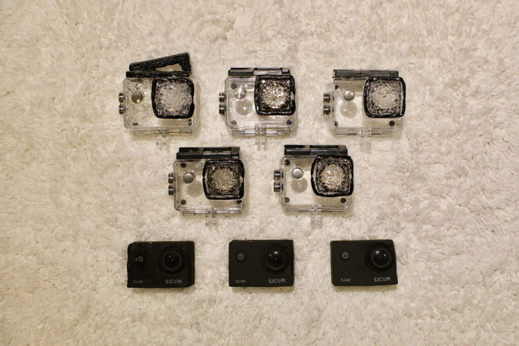 Three cameras and five plastic camera casings are resting on a surface. The camera cases are partially melted.