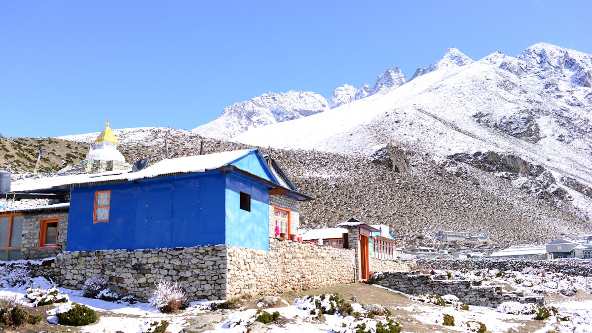 A blue building sits on a stone foundation with snow-covered mountains in the background.