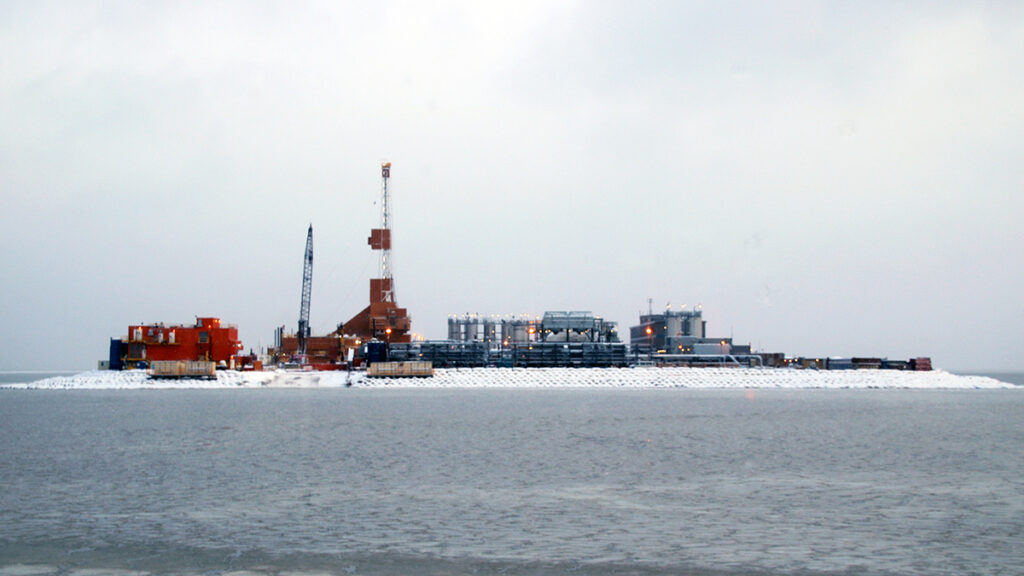 Industrial facilities cover a small island, with gray-blue water in the foreground.