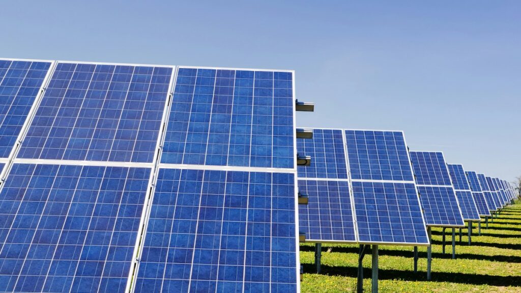 An array of solar panels on a field under a blue sky.