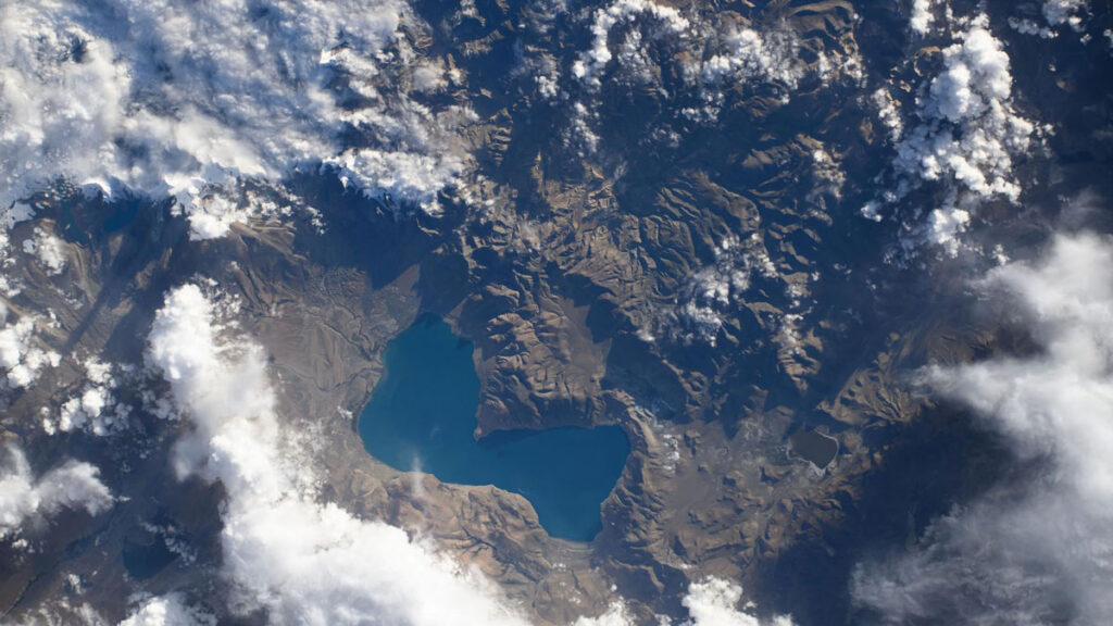 A satellite image shows a mountainous landscape with a blue lake, covered in clouds.