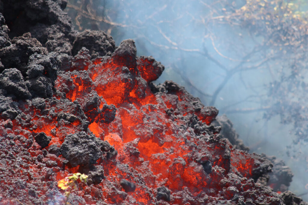 A close-up image of cooling lava glows red. The uppermost layer of smallish pebbles is fading to black.
