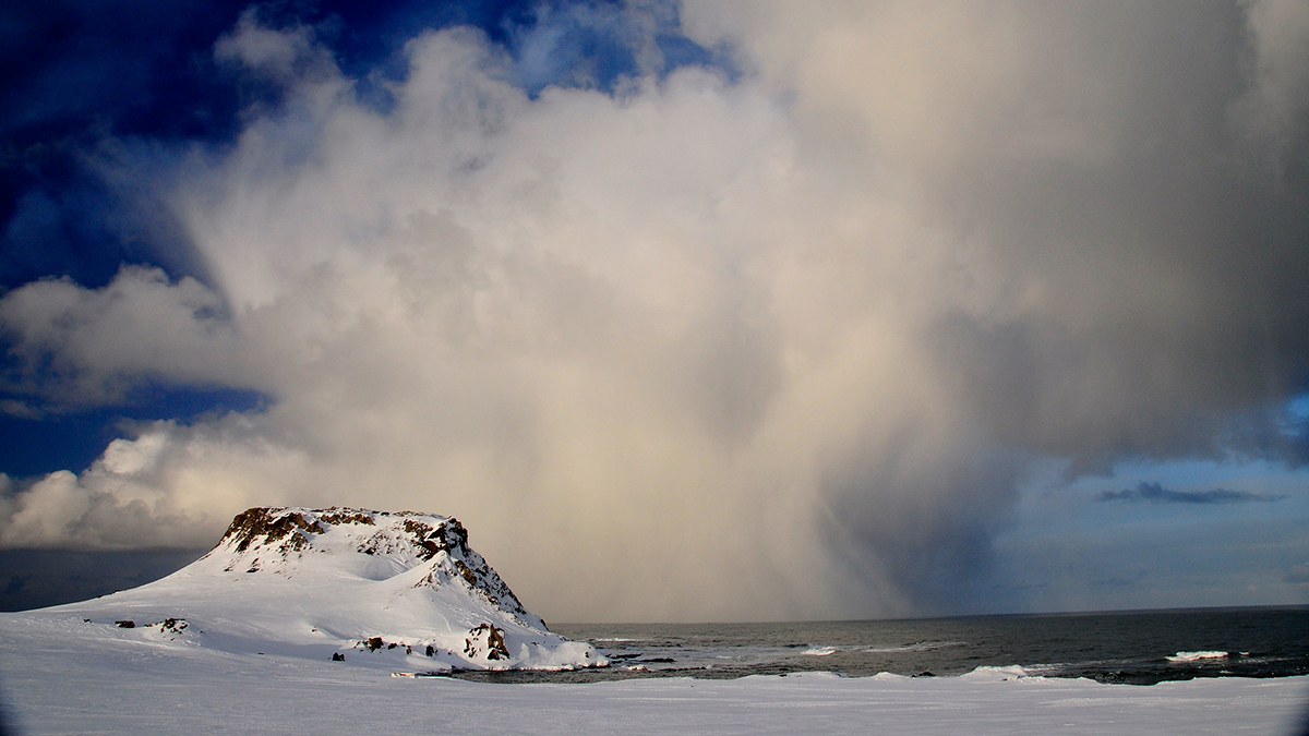 A storm approaches a rocky peak covered in snow in Antarctica.