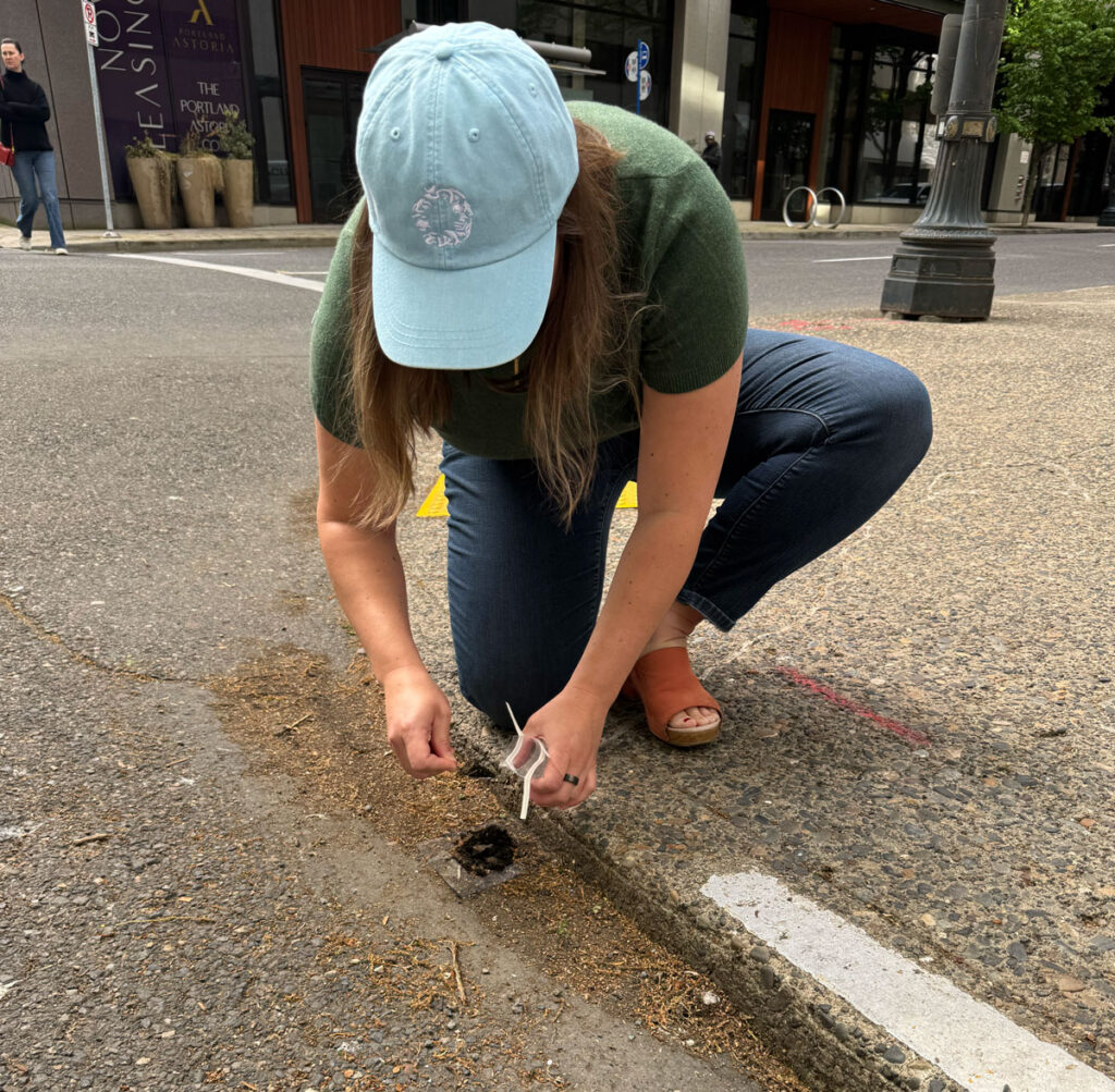 A woman kneels down on a sidewalk to collect a piece of rubber from the street.
