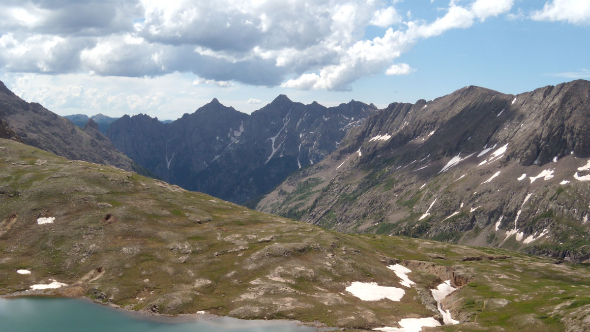 A small lake is seen in the foreground, with a grand mountain range in the background.