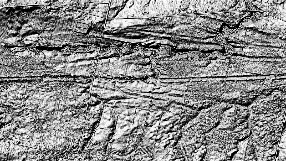A black-and-white image shows long grooves carved into a landscape.
