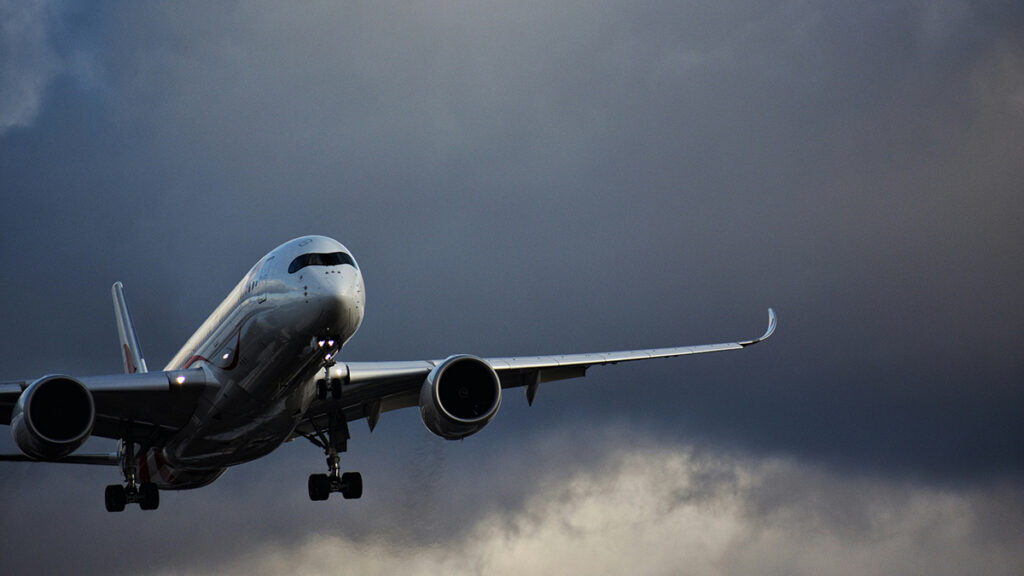 An airplane flies in front of a gray cloud.