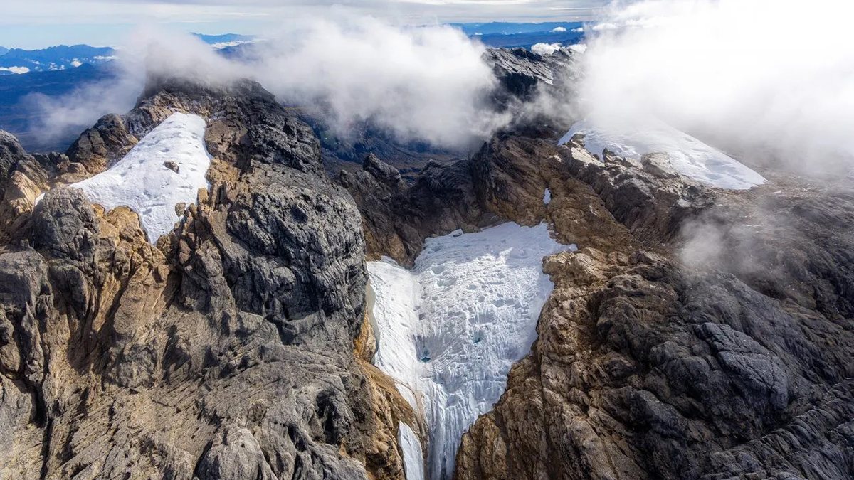 An aerial photo shows three small remnants of glaciers atop a rocky mountain.