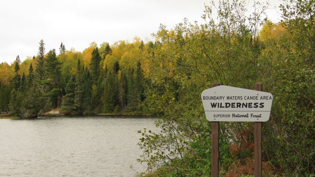 A sign next to a lake in the forest reads “Boundary Waters Canoe Area Wilderness, Superior National Forest.”