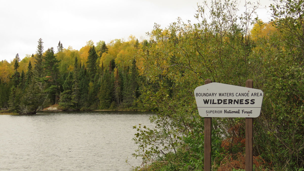 A sign next to a lake in the forest reads “Boundary Waters Canoe Area Wilderness, Superior National Forest.”