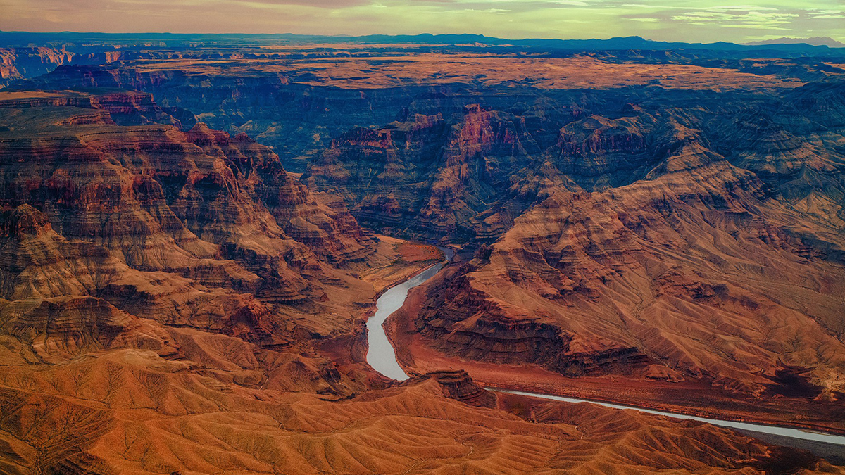 A thin river winds through a landscape of layered red rocks.