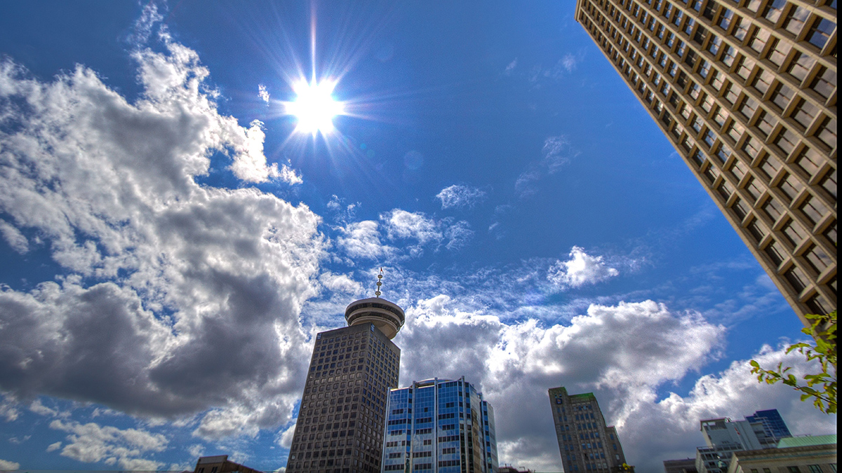 The midday Sun shines amid a scattering of clouds over a city.