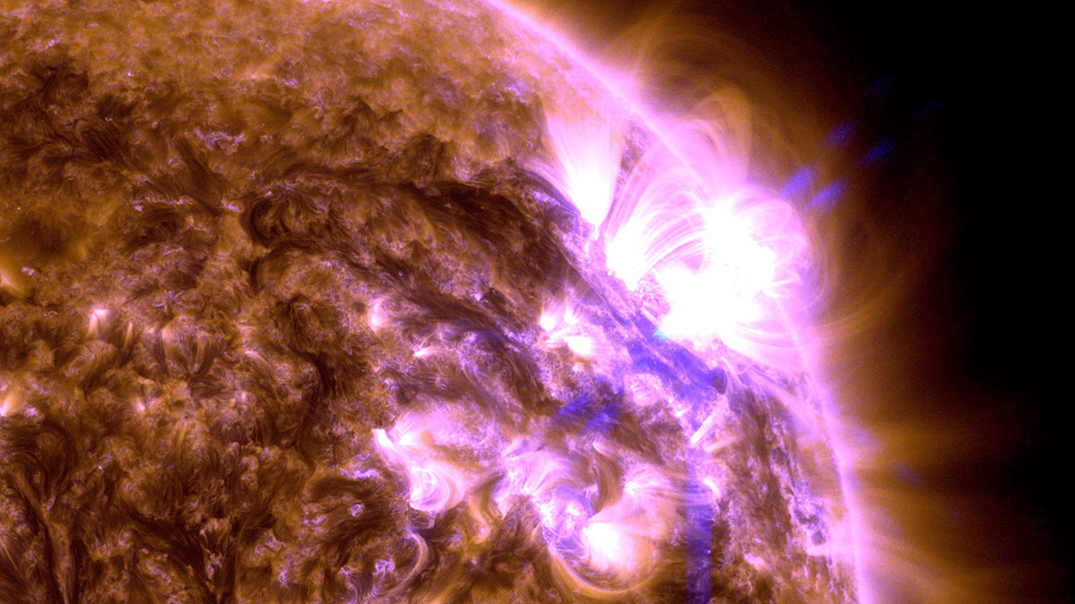 A purplish photo of the Sun shows cords of flame stretching off and arcing back onto its surface.