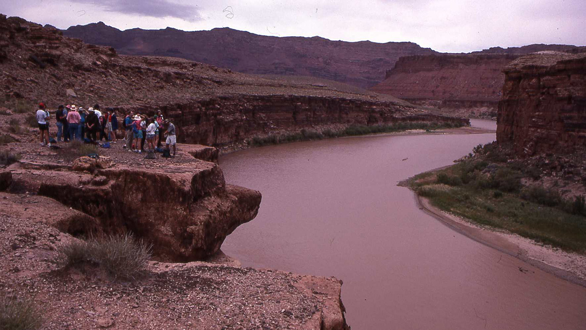 A group of people stand on a rock overlooking a river.