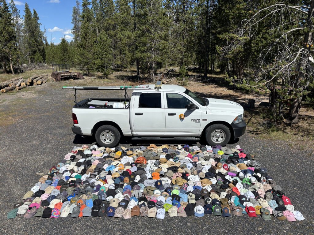 More than 28- hats (mostly baseball caps but also sunhats) are laid out in a rectangle next to a truck. The footprint the hats cover is larger than the truck's.