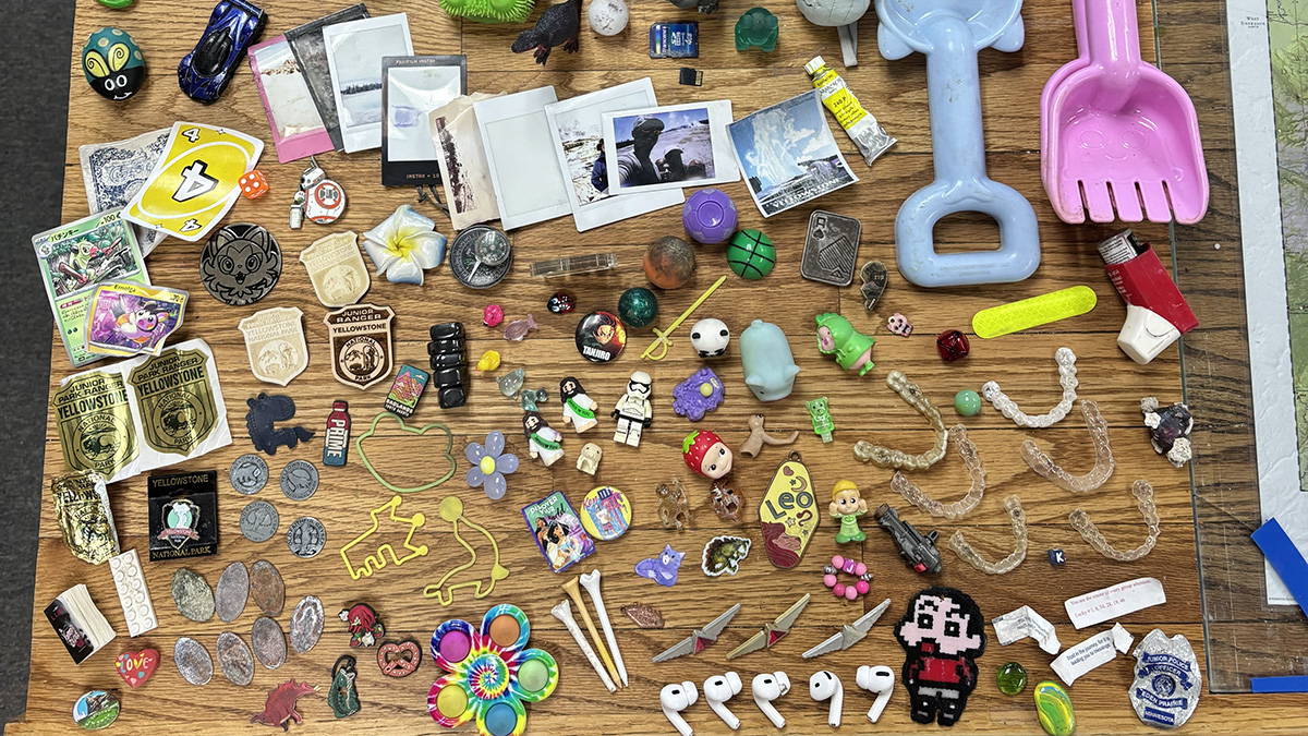 An array of dozens of random objects laid out on a table, including airpods, lego figurines,Invisalign retainers, a fidget spinner, polaraoid photos, toy cars, and plastic shovels.