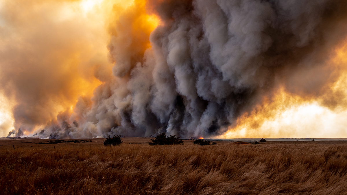 A huge plume of smoke being emitted from a wildfire on a prairie.