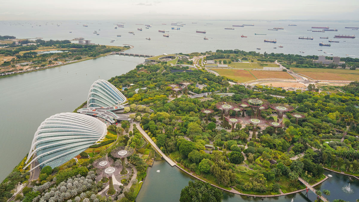 An aerial photo shows two dome-shaped structures along a shoreline. The land is covered in greenery and uniquely shaped buildings. Water stretches out to the horizon.