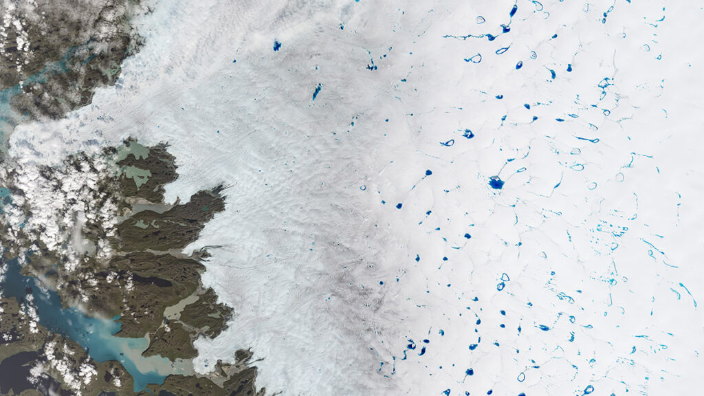 A satellite image of an ice sheet dotted with blue melt ponds. On the left is an area of dirt.