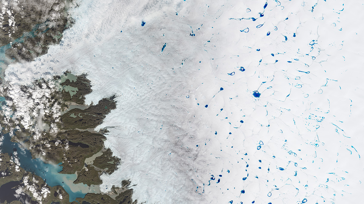 A satellite image of an ice sheet dotted with blue melt ponds. On the left is an area of dirt.