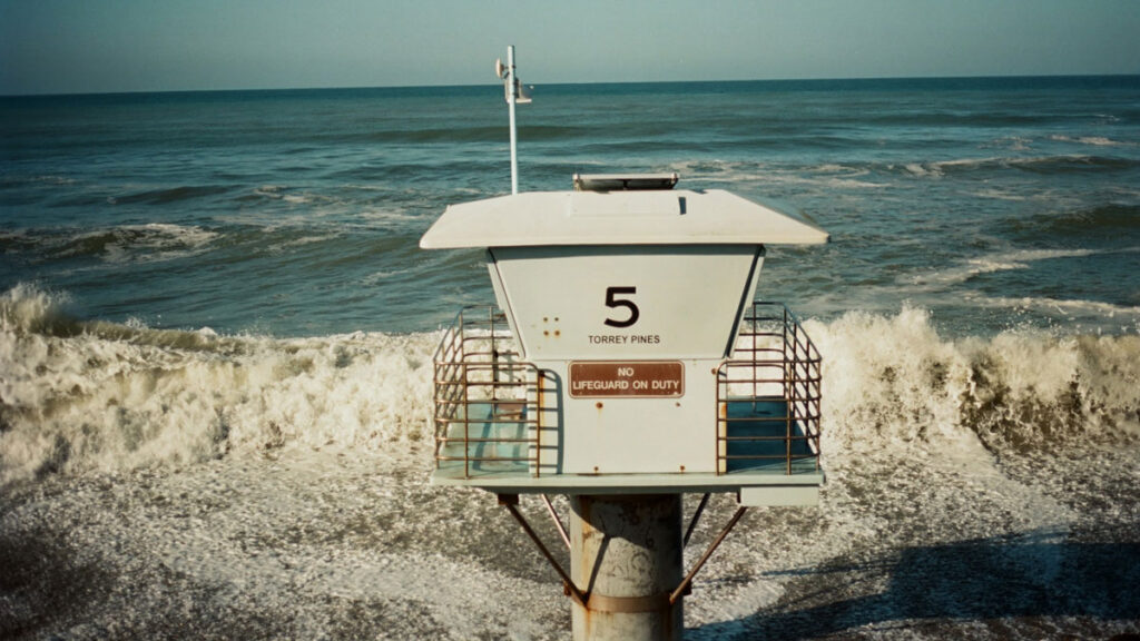 Waves wash up around the base of a lifeguard tower that says “5 Torrey Pines. No lifeguard on duty.”