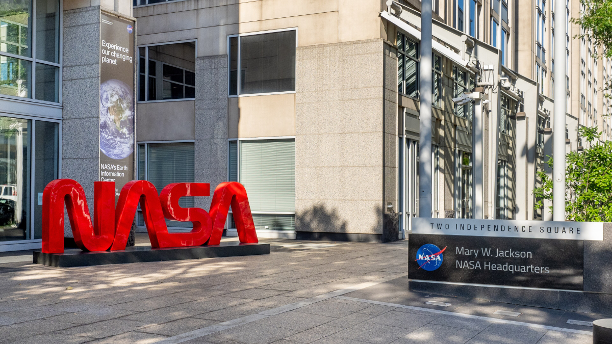 A gray stone building with the red NASA “worm” logo out front and another sign with the NASA “meatball” logo showing it to be the Mary W. Jackson NASA Headquarters in Washington, D.C.