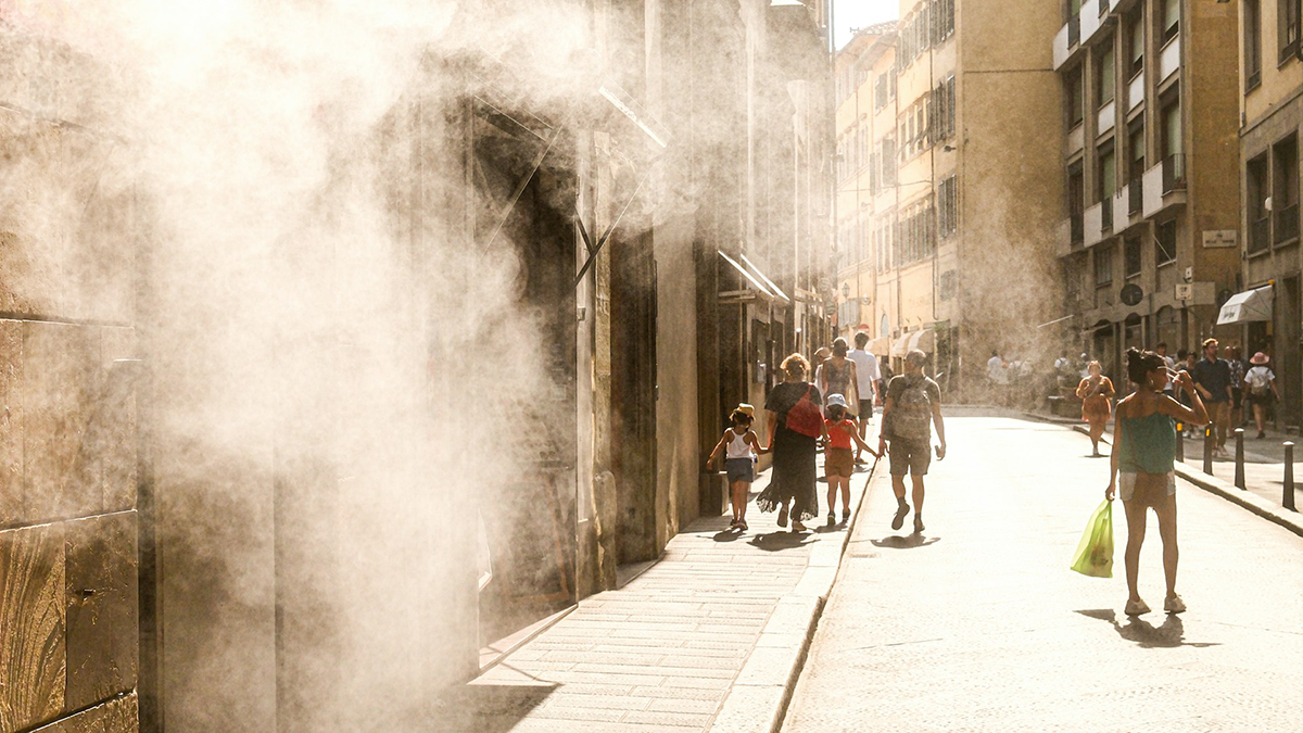People walk down a sunny street with misting spray.