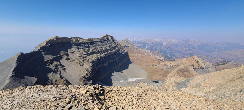 A panoramic view from the summit of a mountain. Many other mountains can be seen in the distance, with a prominent mountain ridge in the foreground.