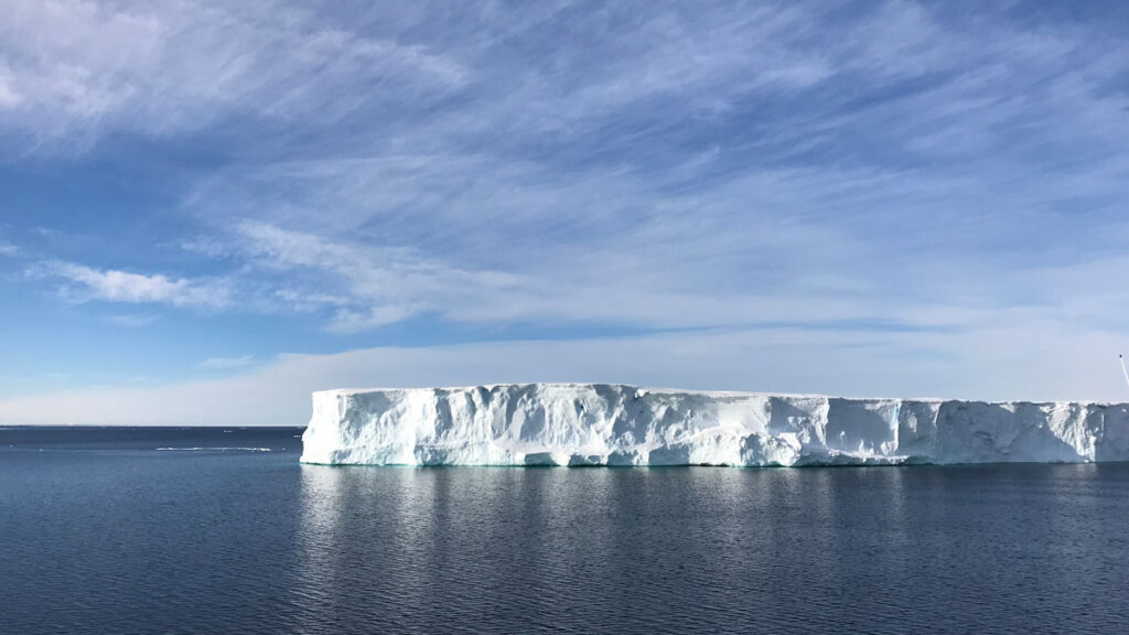 An iceberg floats in blue water.