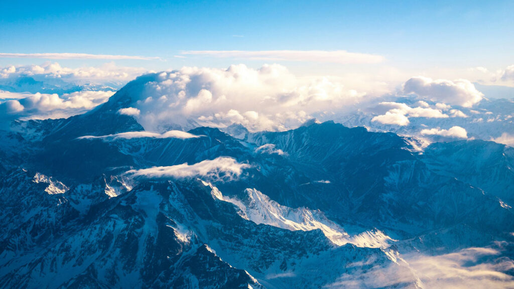 Clouds float over a snowy mountain range, photographed from above by plane.
