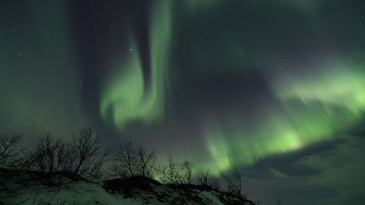 Green swirls of light in the sky above a snow-covered hillside.