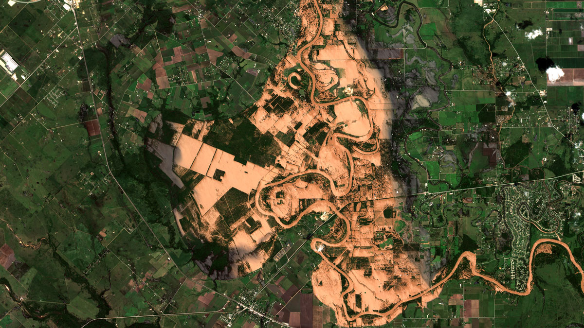 A satellite image shows sediment from winding river extending far beyond its borders. The brown area of sediment is surrounded by green.
