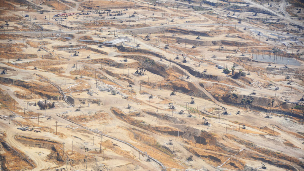 An overhead view of a desert dotted with roads, upright poles, and buildings.