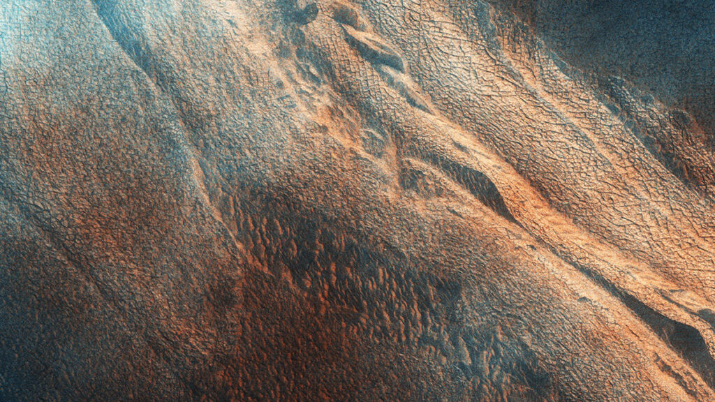 A mottled red and blue surface with ridges, valleys, and cracks. The ridges sweep from top left to bottom right.
