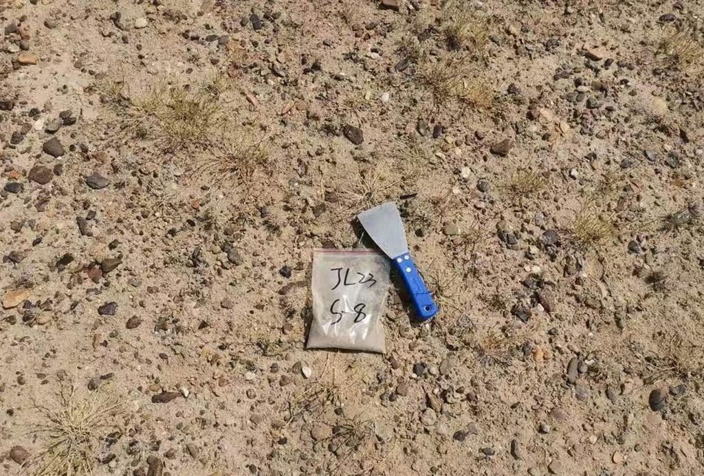 A small plastic bag and a scraper are seen lying in a patch of dirt.