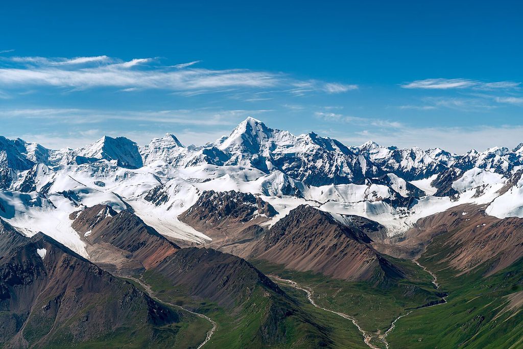 A snowy mountain range in the midground fades to a green valley in the foreground.
